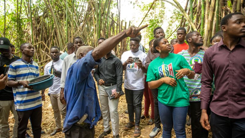 Rita Adjei with other young Africans, some of whom wear Students in Sustainability Action t-shirts, stand outside in a bamboo forest and look where an older man is pointing