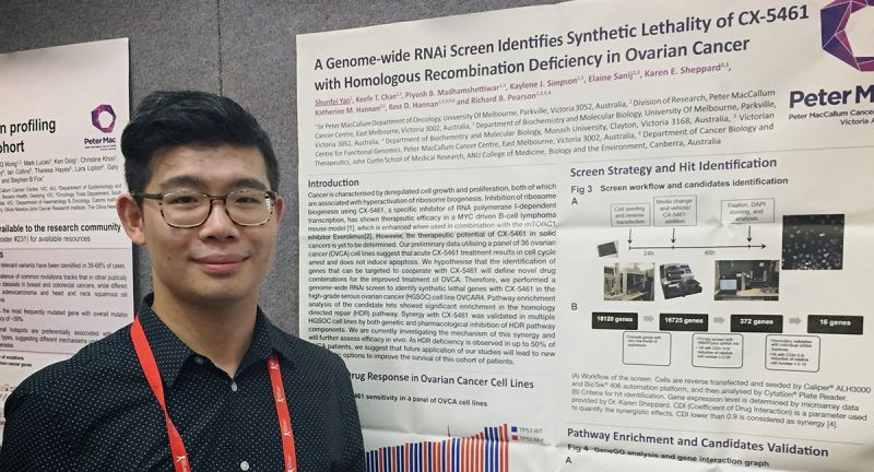 Shunfei Yan, an Asian man with short black hair, next to a poster presenting results from his ovarian cancer PhD research
