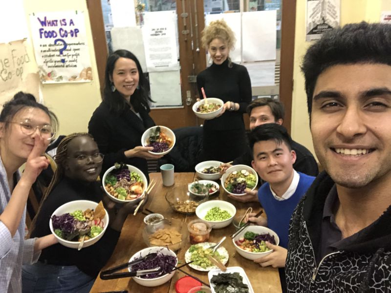 Elaine Pratley, an Asian woman, with a group of happy young people of various ethnicities, sharing food in a small intimate room 