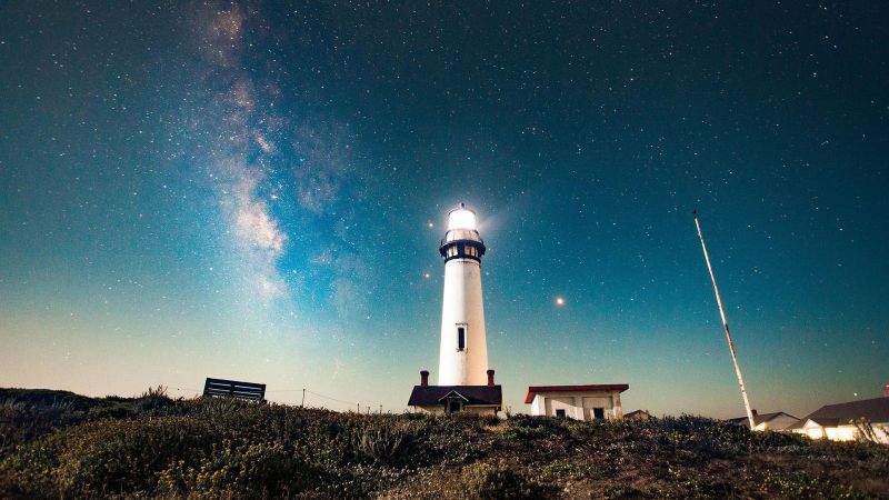 A white lighthouse lit up at night against a starry night background