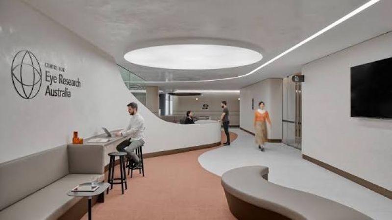 A neutral reception space with people walking through, a man sitting at a laptop and another person behind a receptionist desk