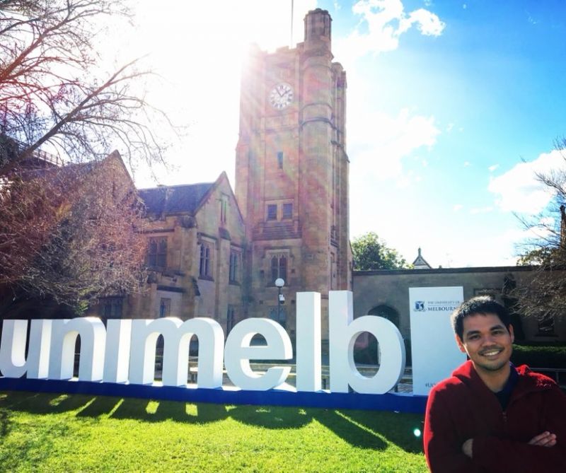 Dr Oscar T Serquina Jr, a Filipino man, stands on a sunny University of Melbourne lawn with 