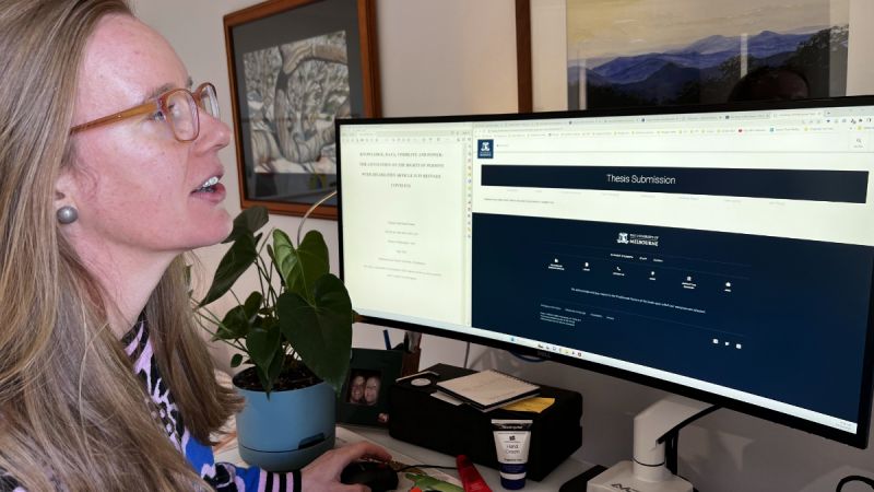 Philippa Duell-Piening sits at a computer, submitting her thesis through a University of Melbourne website