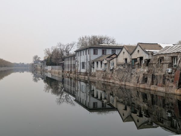 Historic buildings line a canal outside Beijing’s Forbidden City, their reflections mirrored in still water. Modern additions subtly interrupt the traditional facades