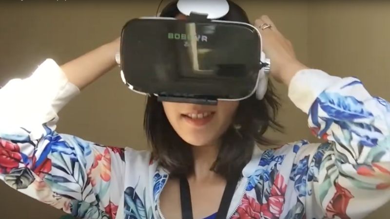 Wearing a colourful sweater, Elaine Pratley pulls a VR headset over her head, obscuring most of her face