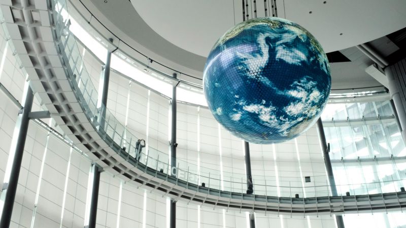 A large building atrium with floor to ceiling glass windows, a curved walkway and large suspended figure of the globe