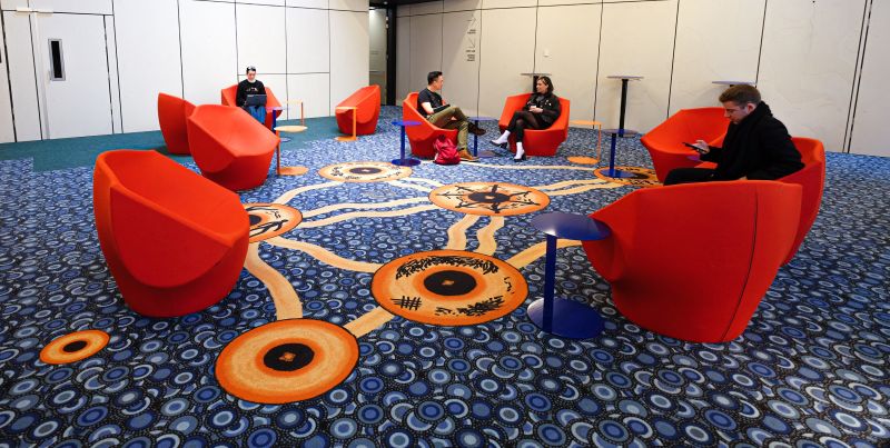 Students on campus in the Arts and Cultural building showing Indigenous design on the carpet