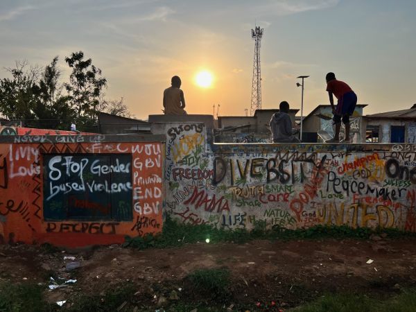 Three young people sitting and standing on a concrete wall covered in grafitti
