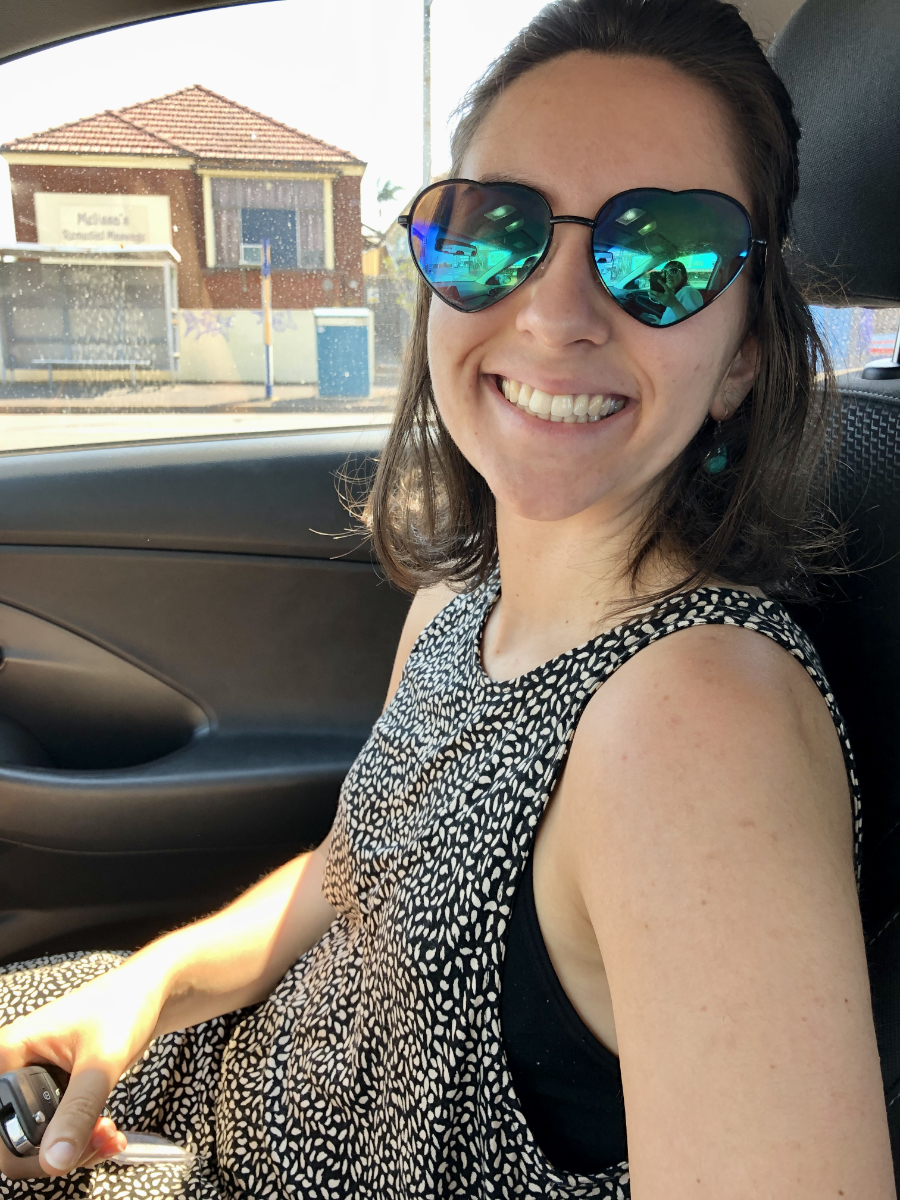 Dr Cristina Tambasco, a light-skinned woman with brown hair grins at the camera in a car, wearing heart-shaped sunglasses