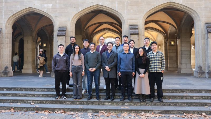 Tairu Chen's research group, people of various genders and ethnicities, wear neat clothing and pose on the stairs in front of a University of Melbourne sandstone building
