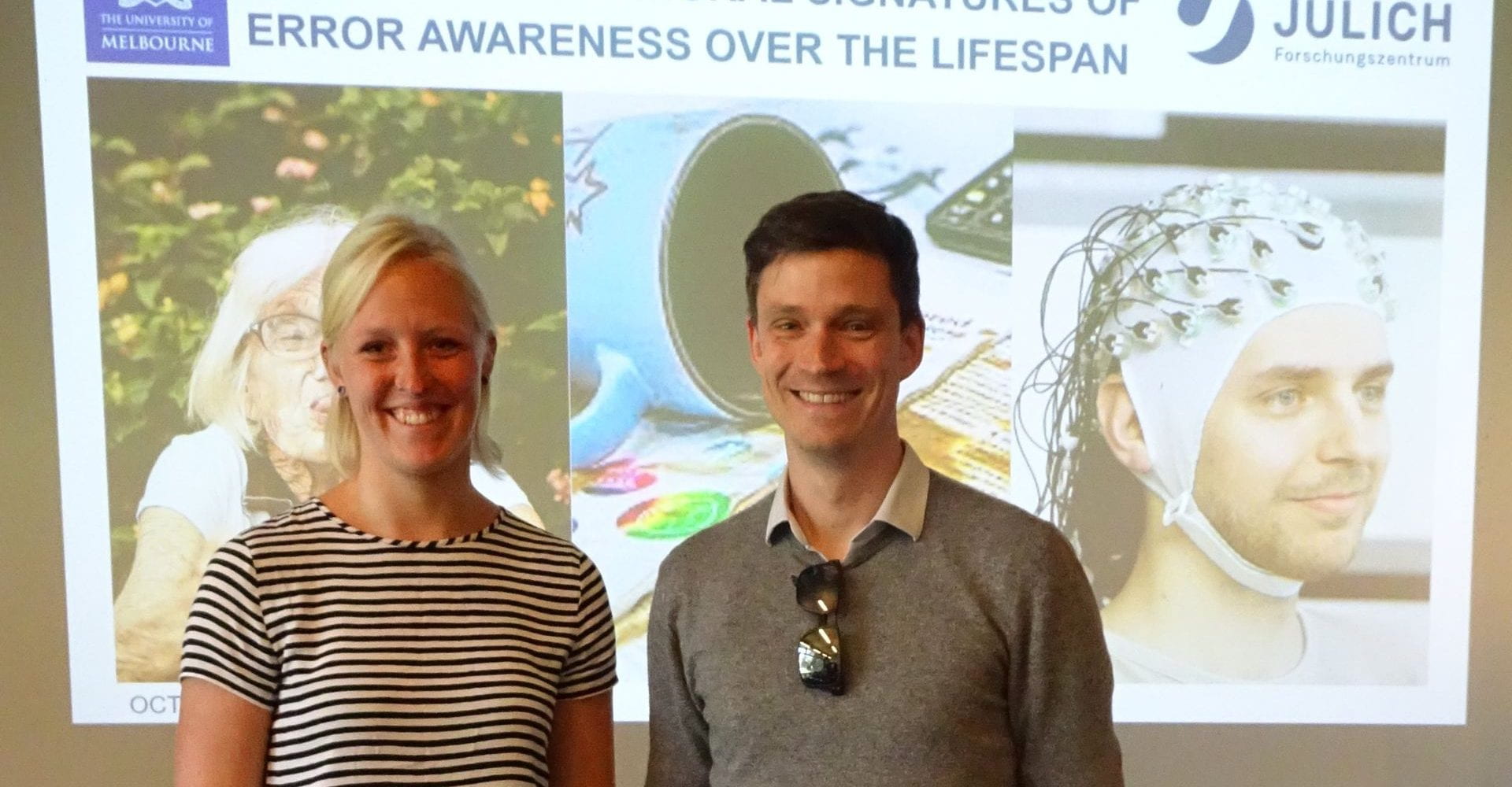 Stefan Bode smiling next to Helen Overhoff with a powerpoint title slide in the background