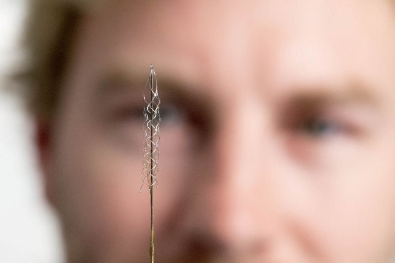 Man holding small silver Stentrode implant device in front of his face