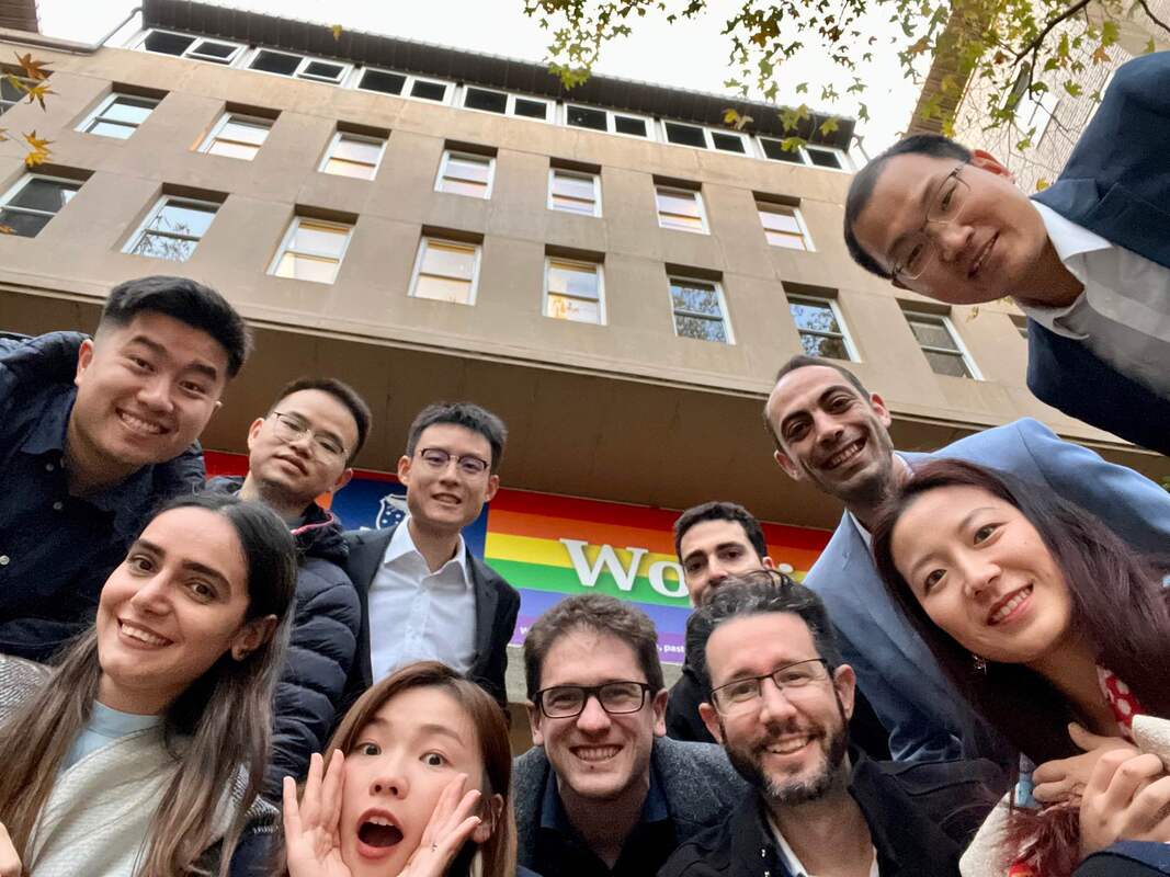 Tairu Chen's researc group - a group of people of various genders and ethnicities cluster around a camera pointing up at them, beaming