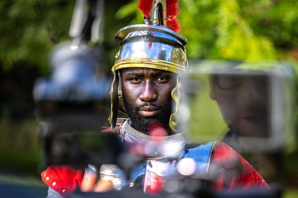This photo captures a moment between takes during a production shoot by the Video and Media team at the University of Melbourne, Parkville (located on the traditional lands of the Wurundjeri Woi‑wurrung people of the Kulin Nation). Actor Kwasi Darko is seen in Roman costume, showing concentrated intensity between the delivery of lines.