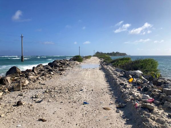 This scene depicts the lowest-lying point on the Ebeye causeway, where the Pacific ocean is lapping over the thin strip of land into the lagoon of Kwajalein, the world's largest Atoll, in the Ralik chain of the Marshall Islands.