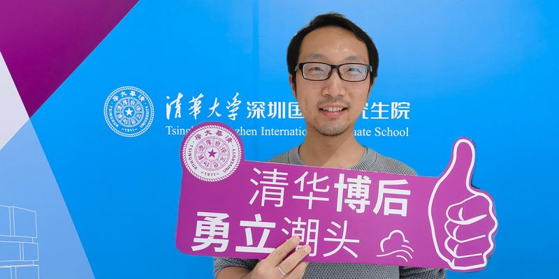 Dr Hanchao Hou smiles while posing with Tsinghua University promotional material