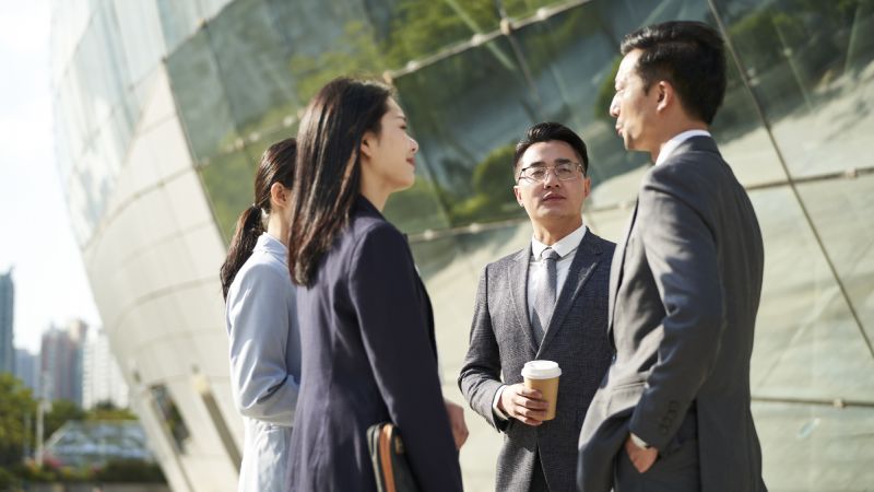 Four Asian people in business attire chat outside