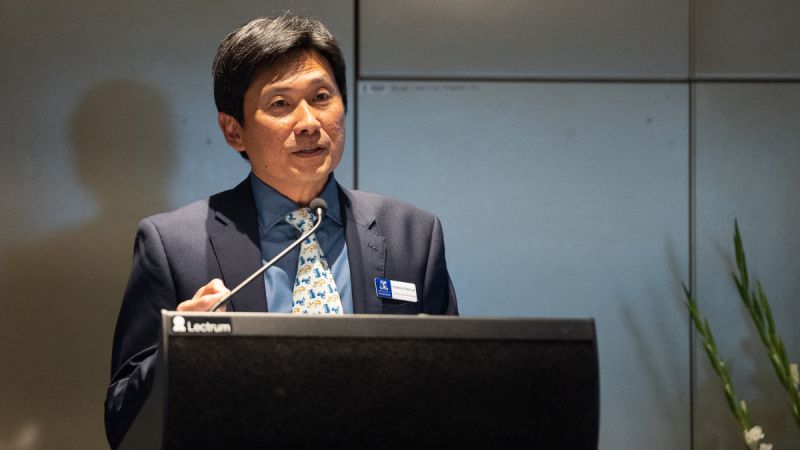 Peter Lee, an Asian man with short black hair and in a neat suit, talks to an audience behind a lectern