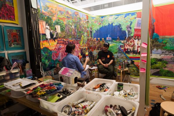 This photograph portrays an artist interview between Indonesian artist Zico Albaiquni and Dr Eliza O’Donnell in Zico’s studio at the Victorian College of the Arts, University of Melbourne, on the Traditional Lands of the Wurundjeri Woi-wurrung and Bunurong / Boon Wurrung peoples of the Kulin Nation. Surrounded by large-scale paintings, works in progress, paint materials, notes, and recording equipment, the image captures the studio as a living research site where artistic practice, material knowledge, cultural memory, and diasporic identity are explored through conversation.