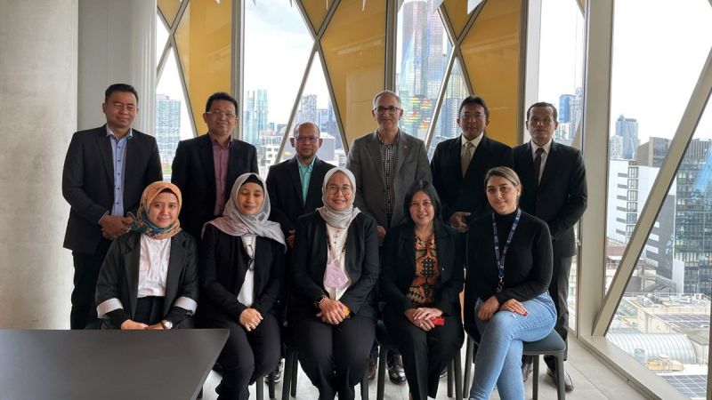 A group of people in formal attire, including Indonesian officials and University of Melbourne researchers, poses in front of a window that opens to the Melbourne CBD