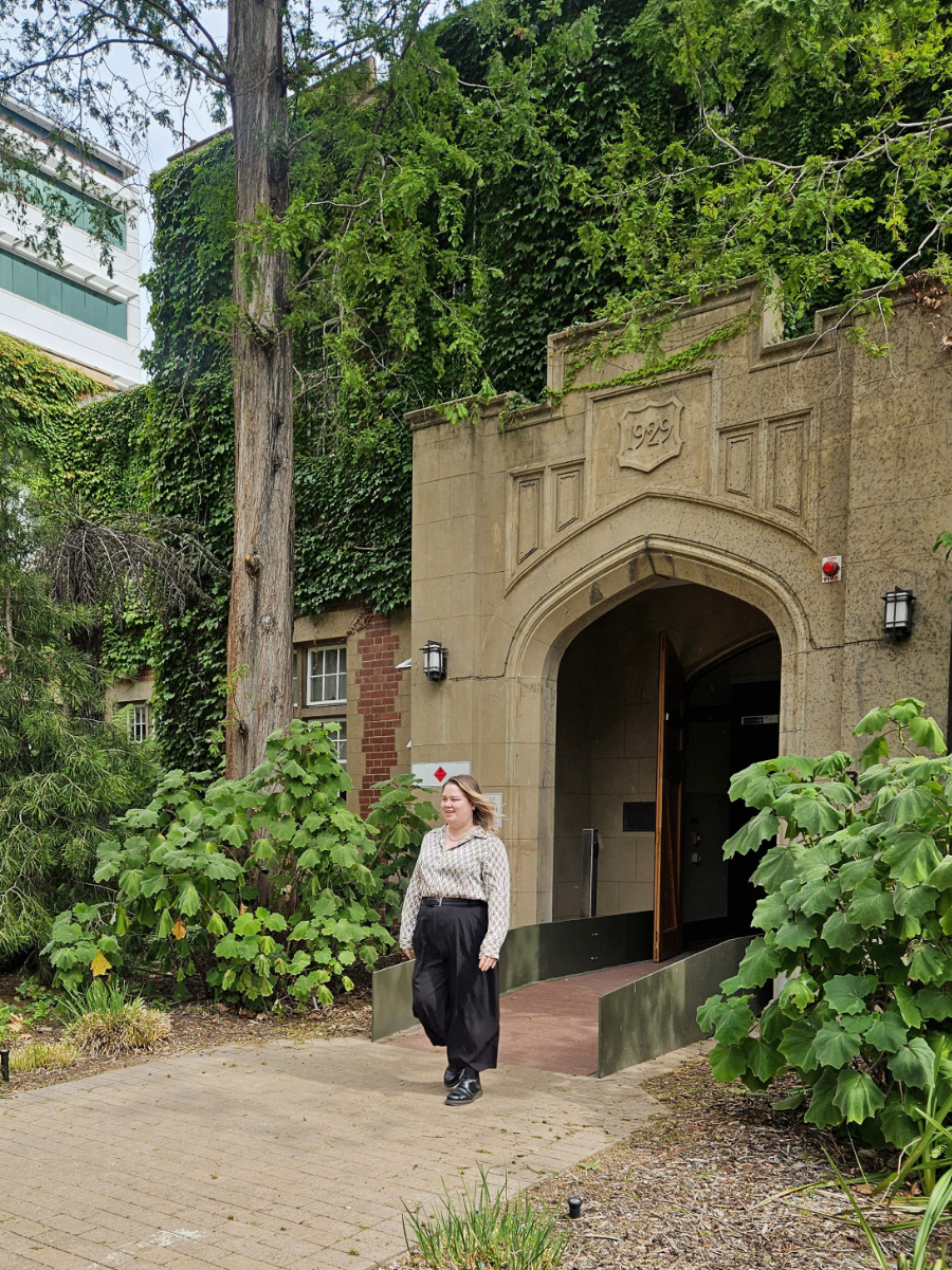 Julia Hall walks out of a sandstone building covered in vines but with 1929 visible on its facade