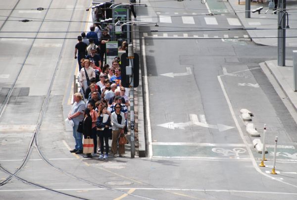 A crowd of people waiting at a tram stop in the middle of a large empty road
