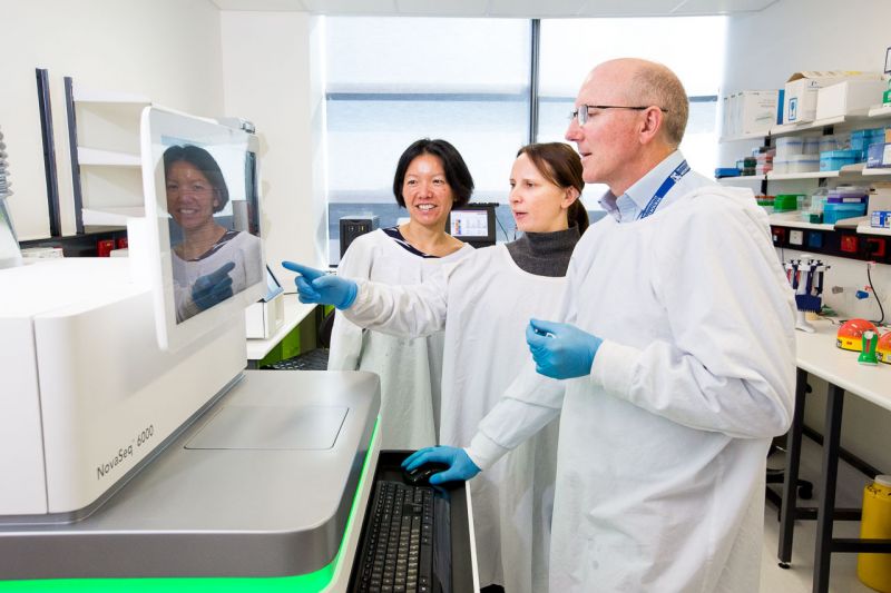 Three scientists in laboratory wearing white lab coats looking at a screen