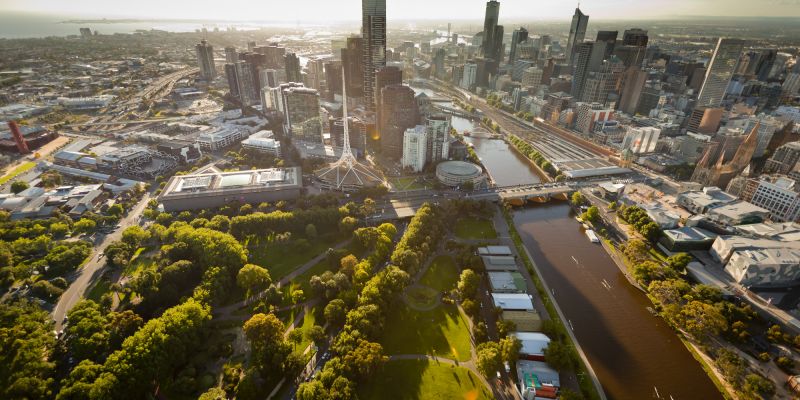 The brown Yarra-Birrarung river flows through central Melbourne while its skyscrapers and the Arts Center are lit in dramatic afternoon light